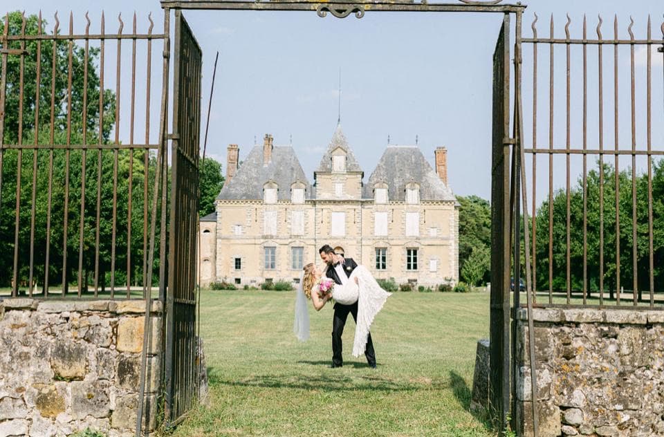 Jeunes mariés devant la façade du château de Motteux, vus depuis le portail en fer forgé du parc