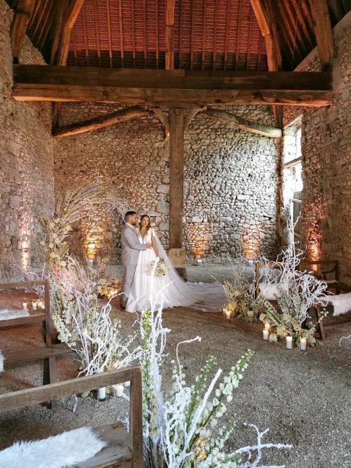 Cérémonie de mariage dans la grange en pierre du château de Motteux, décor floral blanc et bougies